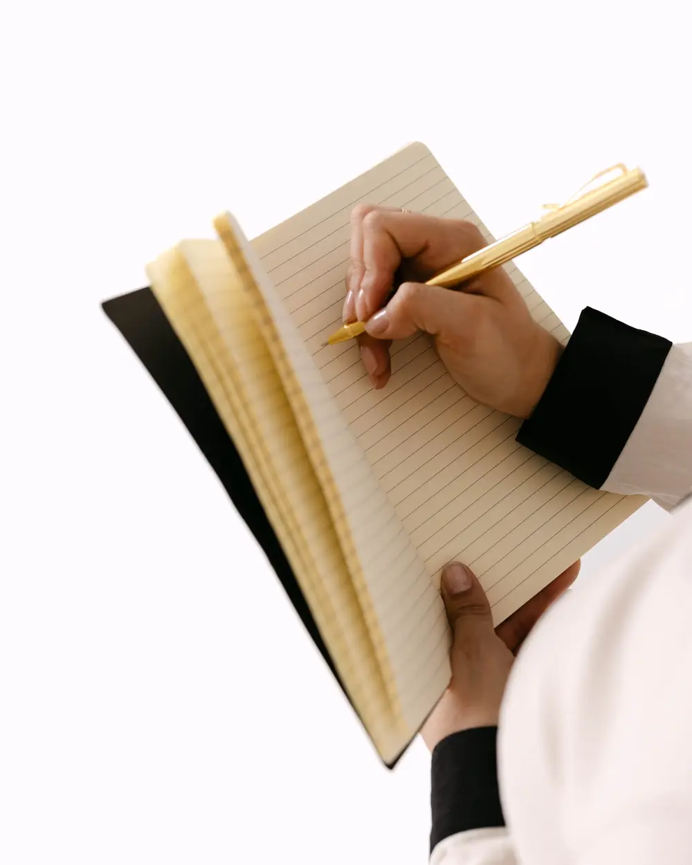A hand writing in a notebook with a gold pen
