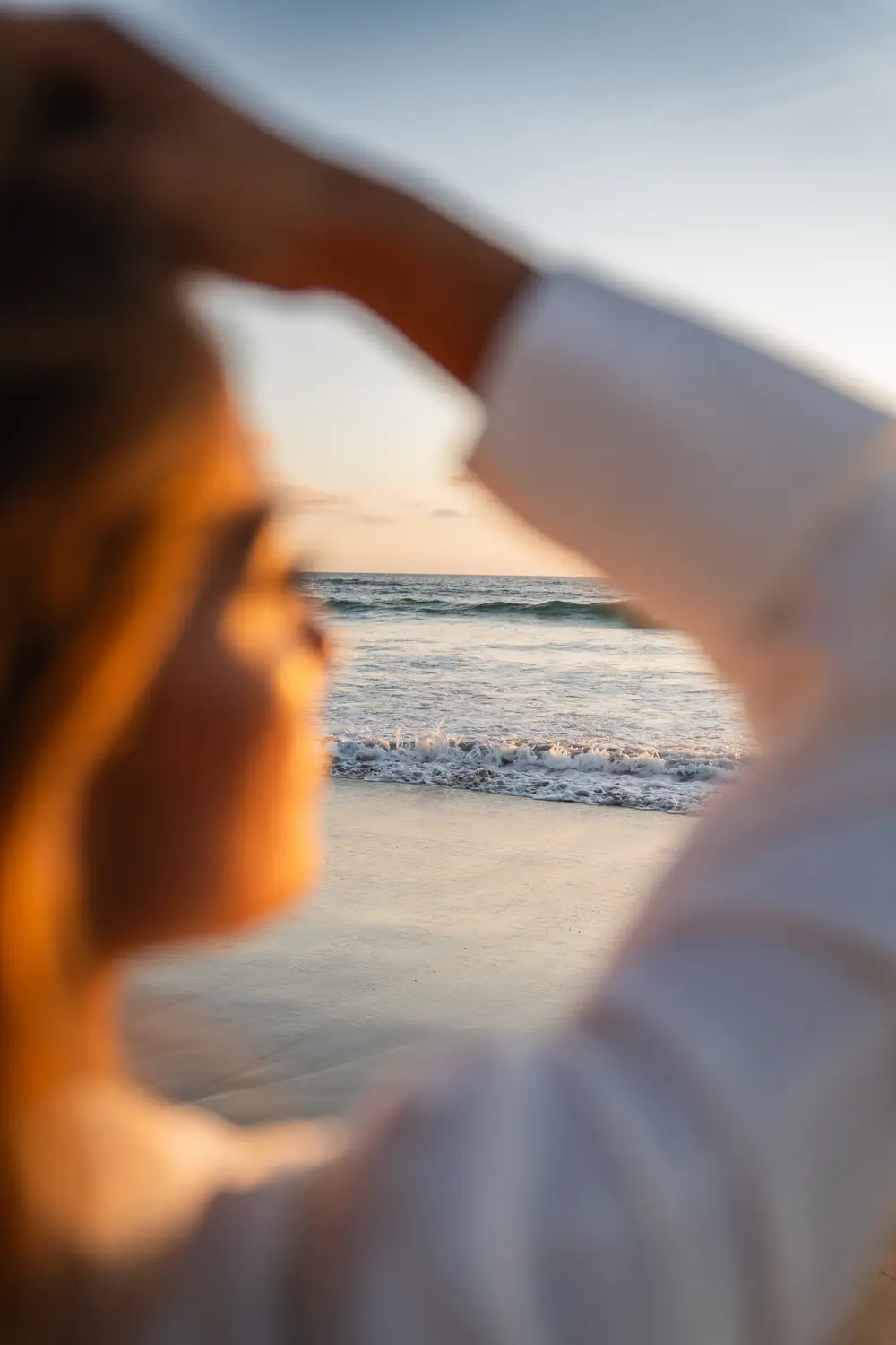 A woman shading her eyes at the beach at sunset